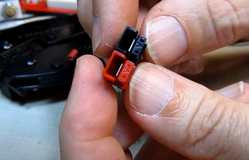 Close-up of a person holding a red and black Anderson Powerpole connector for Bioenno Power battery systems, showing polarized housing for secure DC power connections.